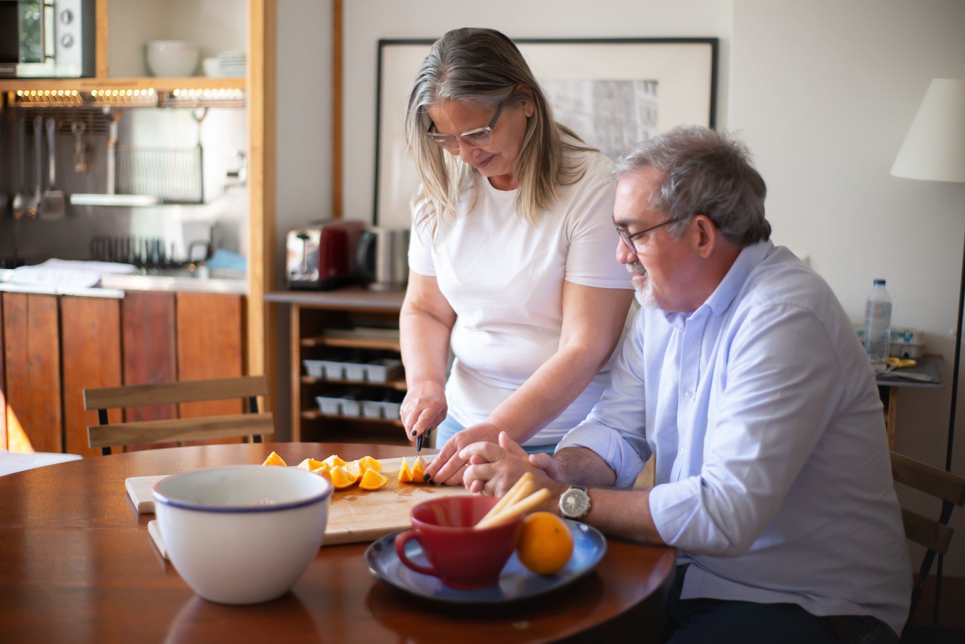 A man and a woman are sitting at a table cutting oranges on a cutting board.
