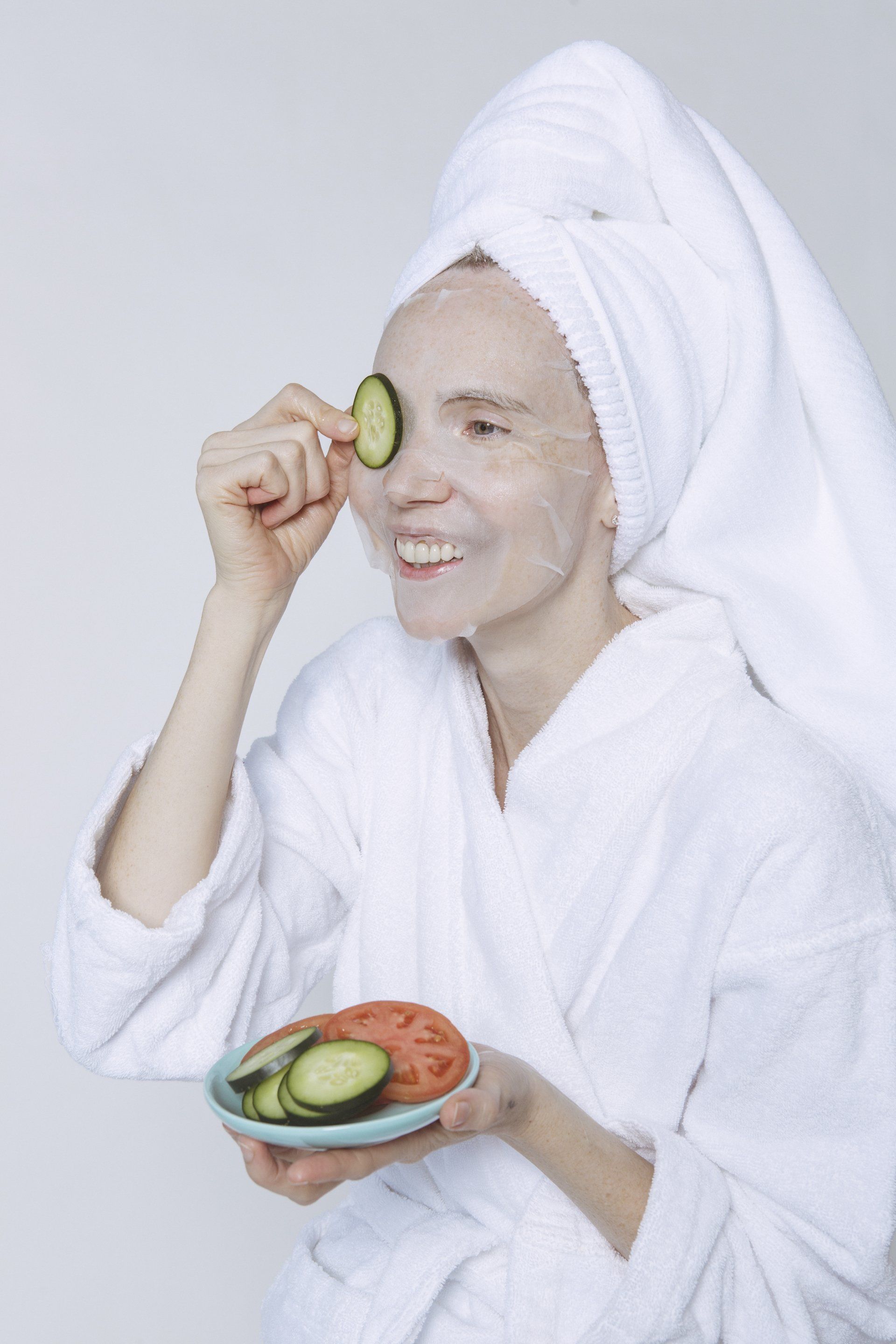 A woman in a bathrobe with a towel wrapped around her head is holding a plate of vegetables.