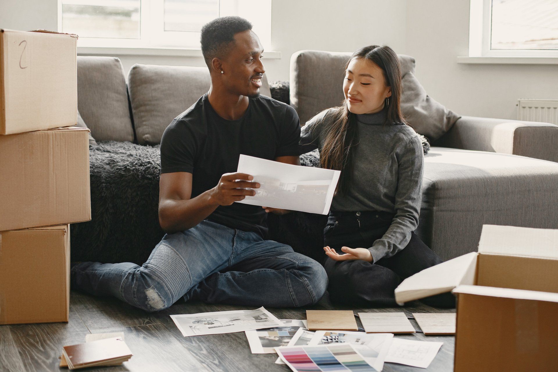 A man and a woman are sitting on the floor in a living room looking at a piece of paper.