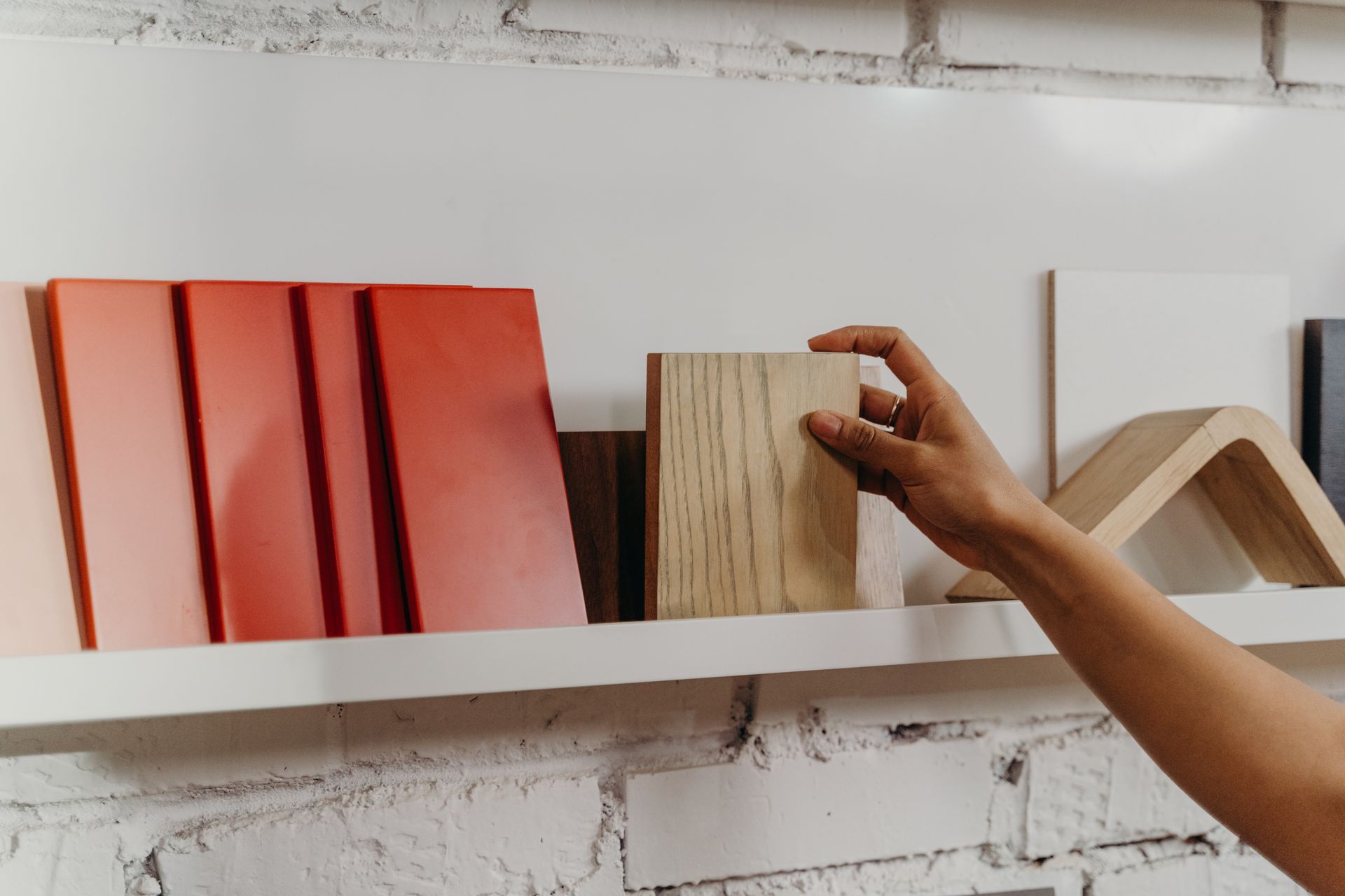 A person is reaching for a piece of wood on a shelf.