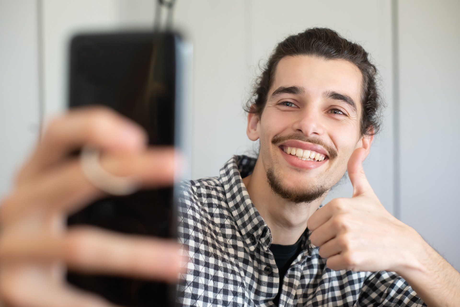 A man is taking a selfie with his cell phone and giving a thumbs up.