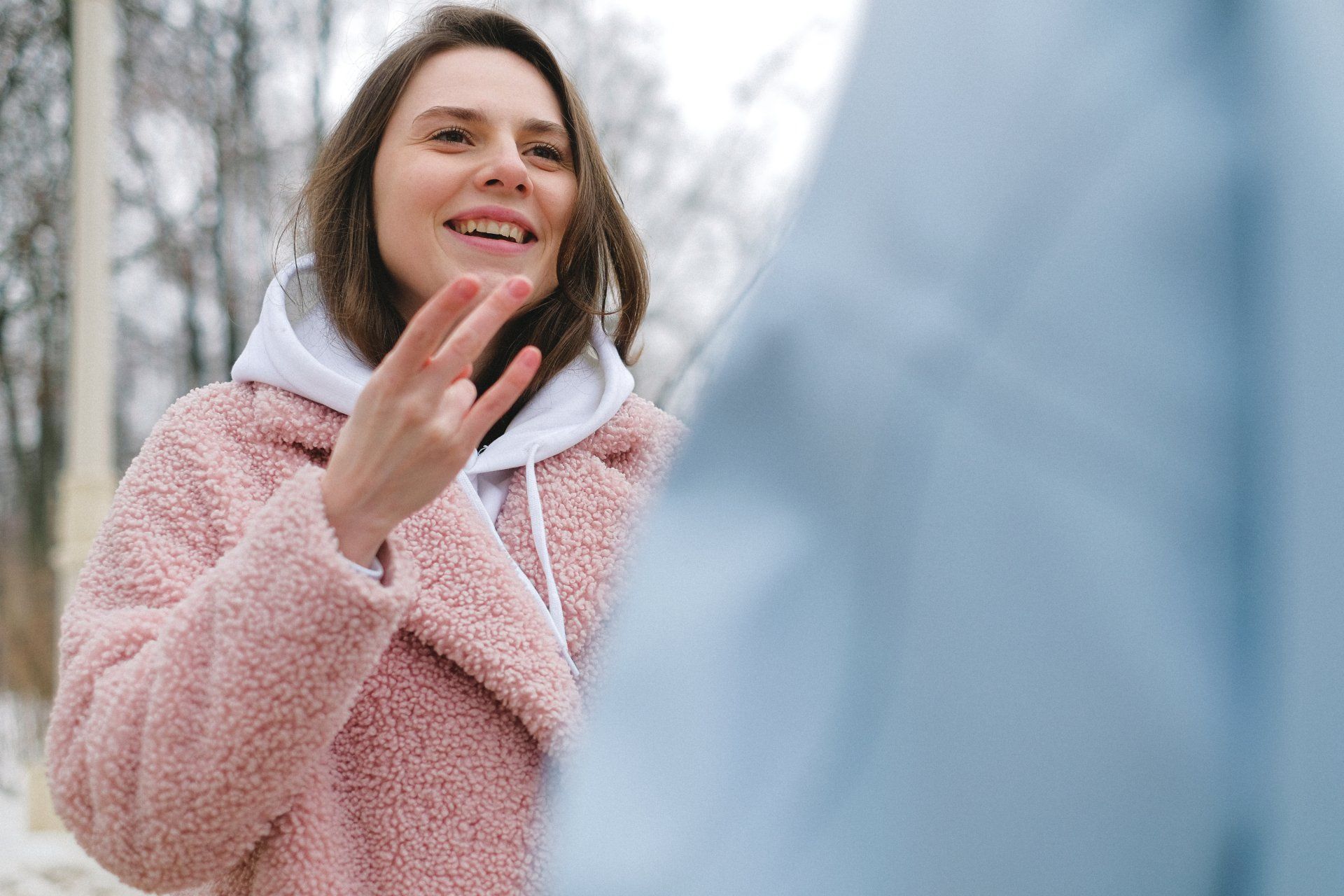 A woman in a pink coat is waving at a man in a blue jacket.