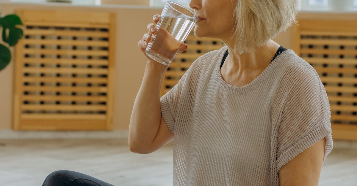 Woman with blonde hair sitting, drinking water from a glass.
