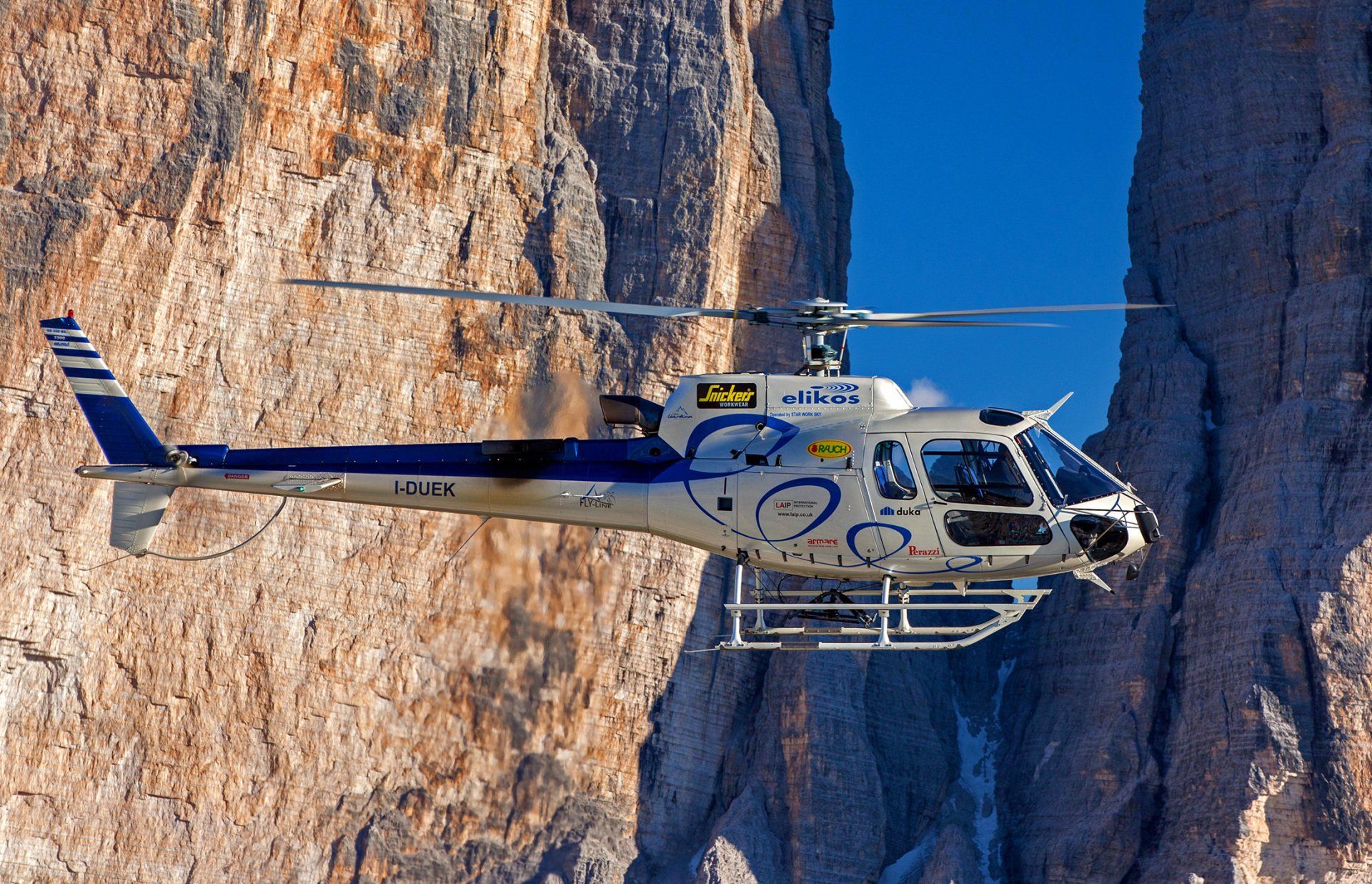 A blue and white helicopter is flying over a mountain