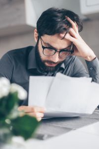 A man with glasses is sitting at a table reading a piece of paper.