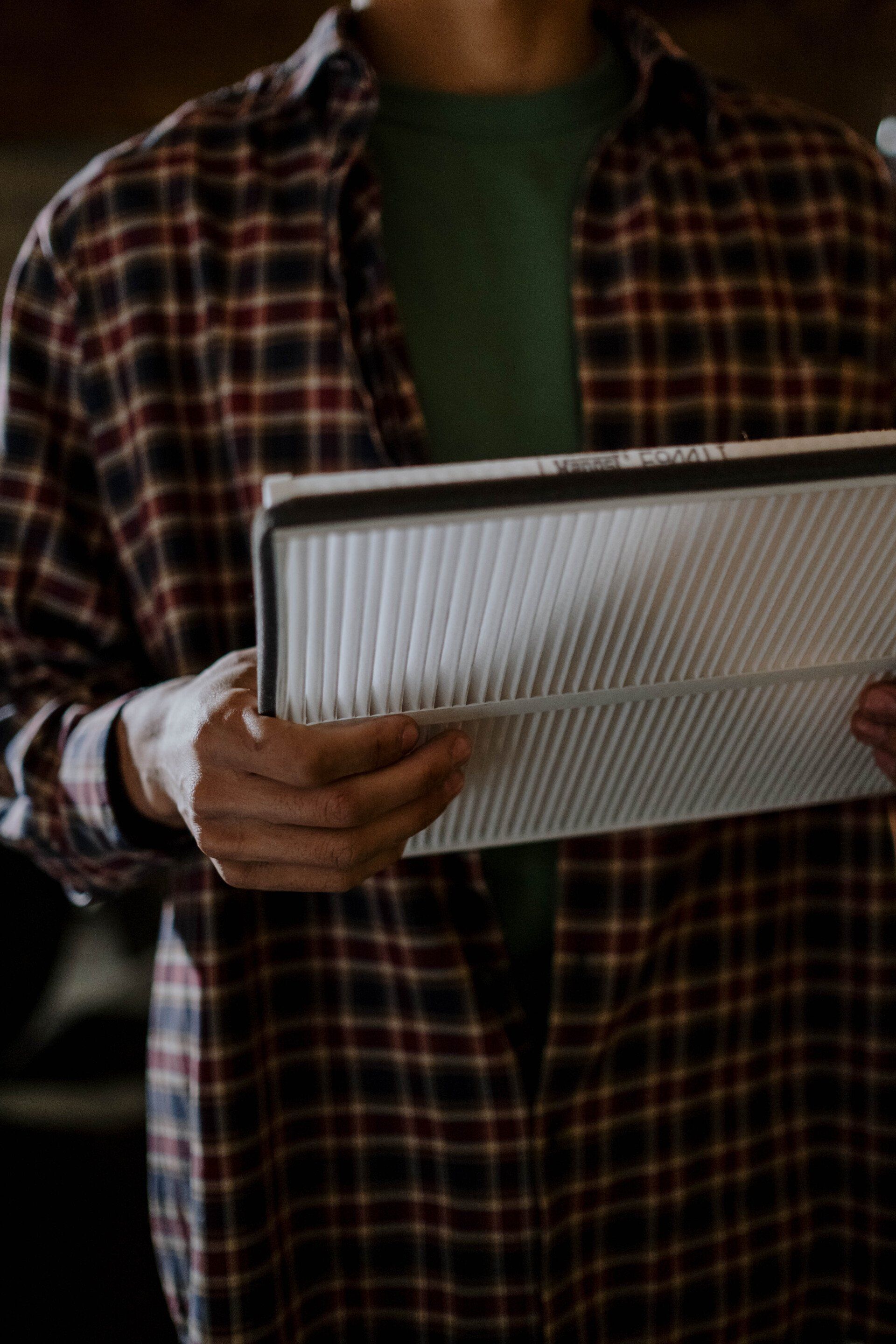 a man in a plaid shirt is holding a piece of air filter in his hands .