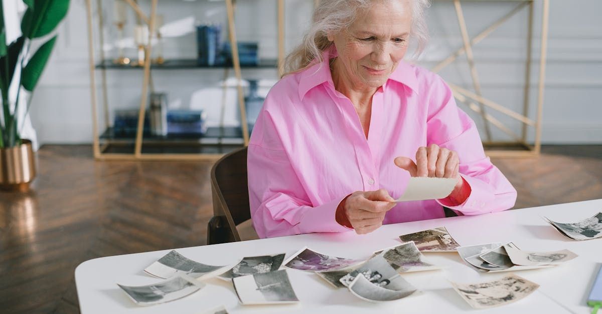 An elderly woman is sitting at a table looking at old photos.