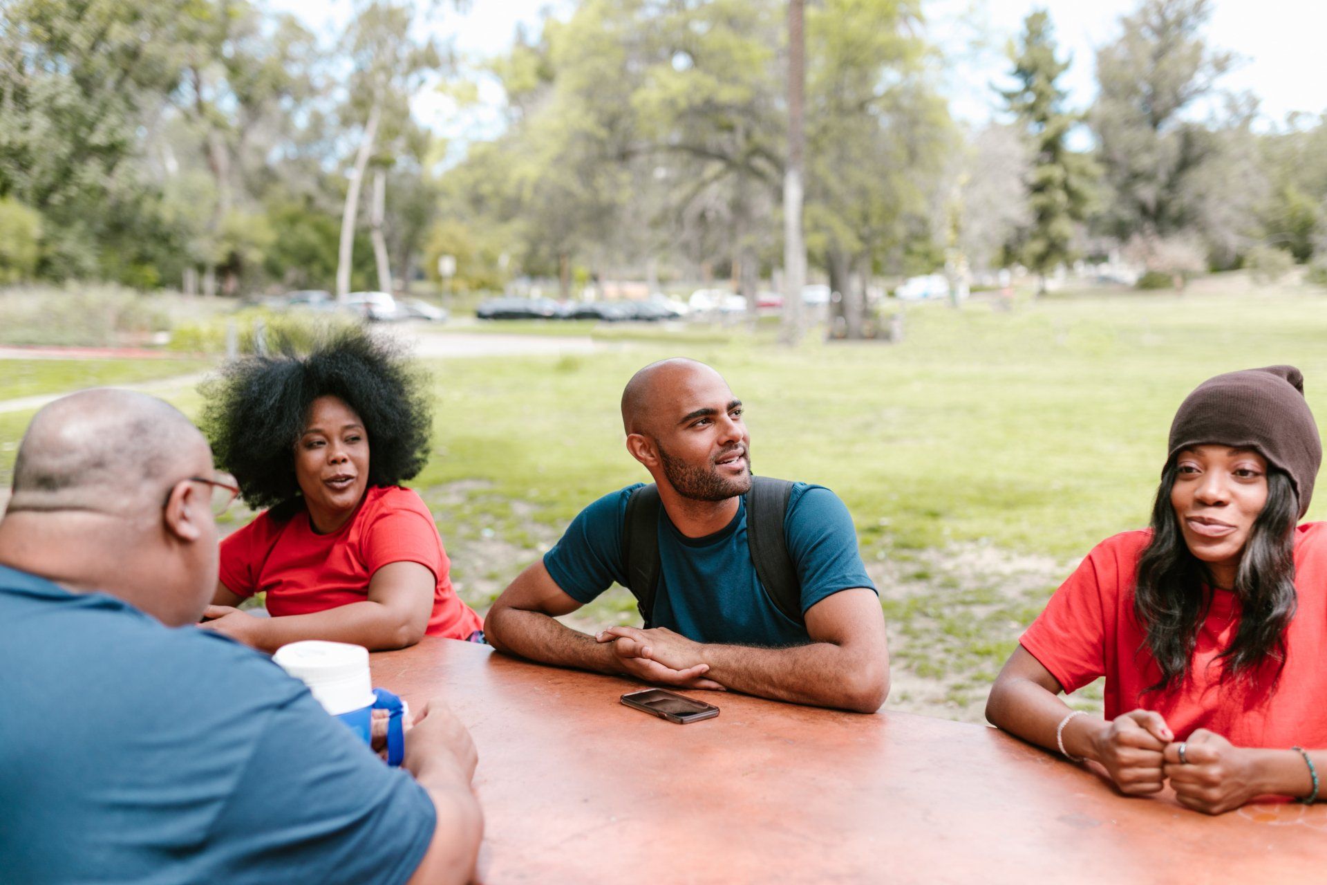 A group of people are sitting at a table in a park.