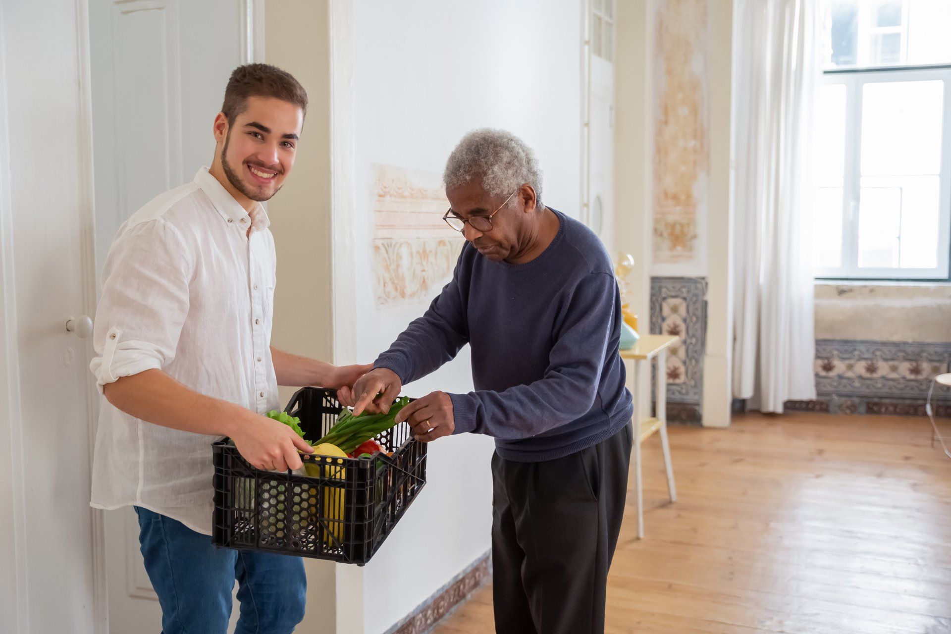 A young man is giving an older man a basket of vegetables.