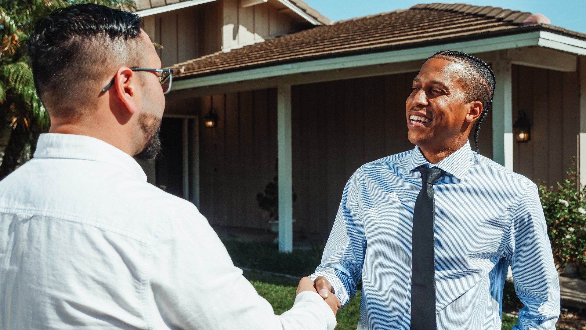 Two men are shaking hands in front of a house.