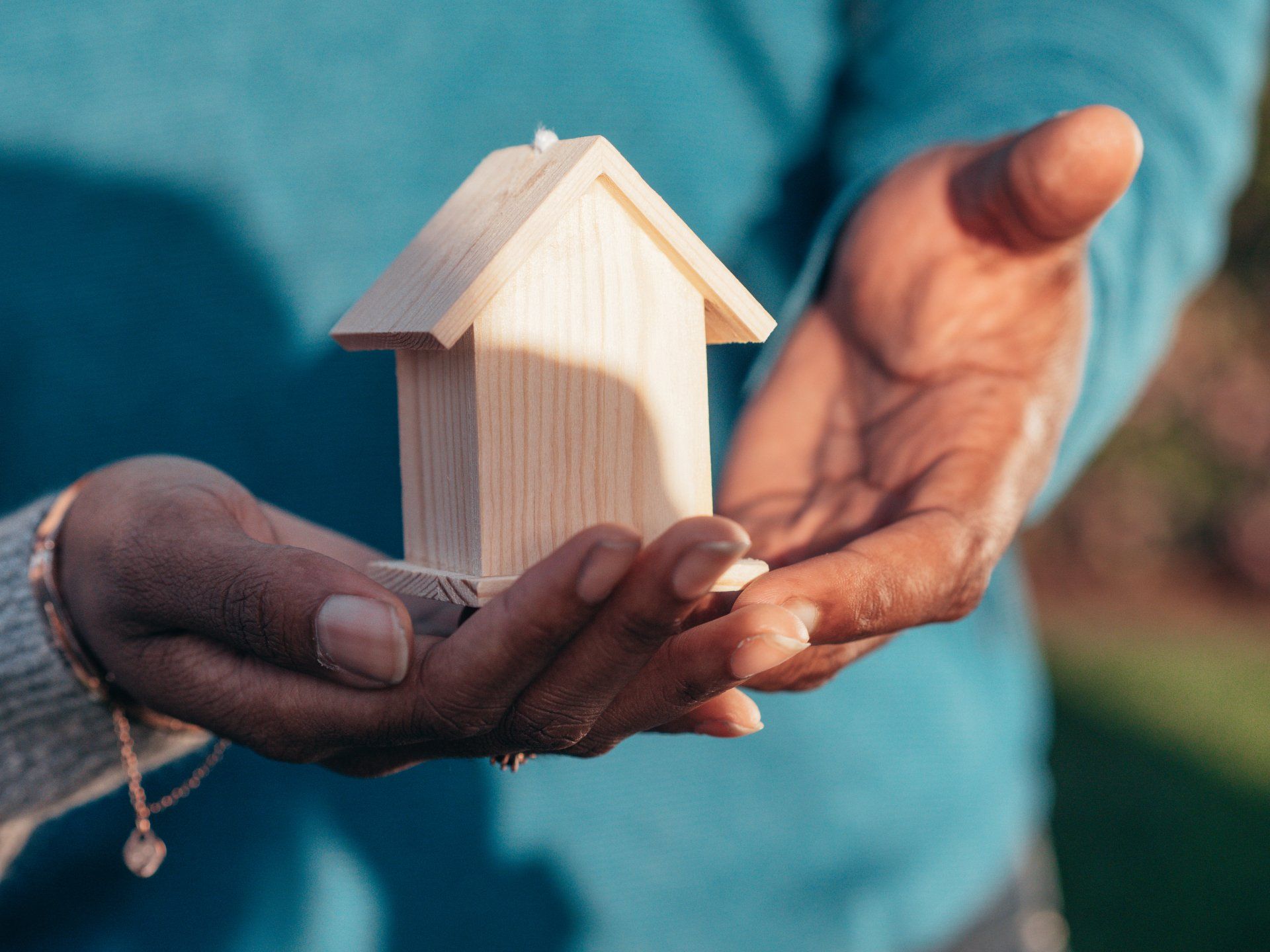 Hands holding a small wooden house model against a blue shirt background