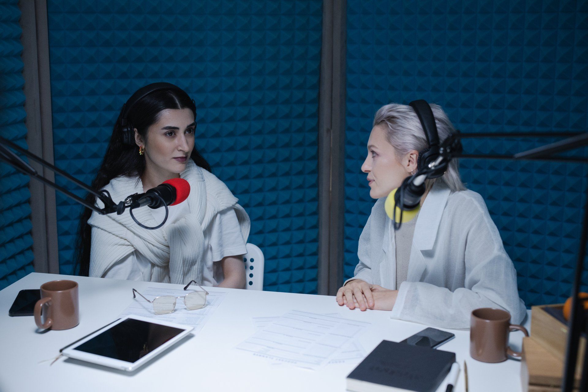 Deux femmes sont assises à une table et parlent dans des micros dans un studio.