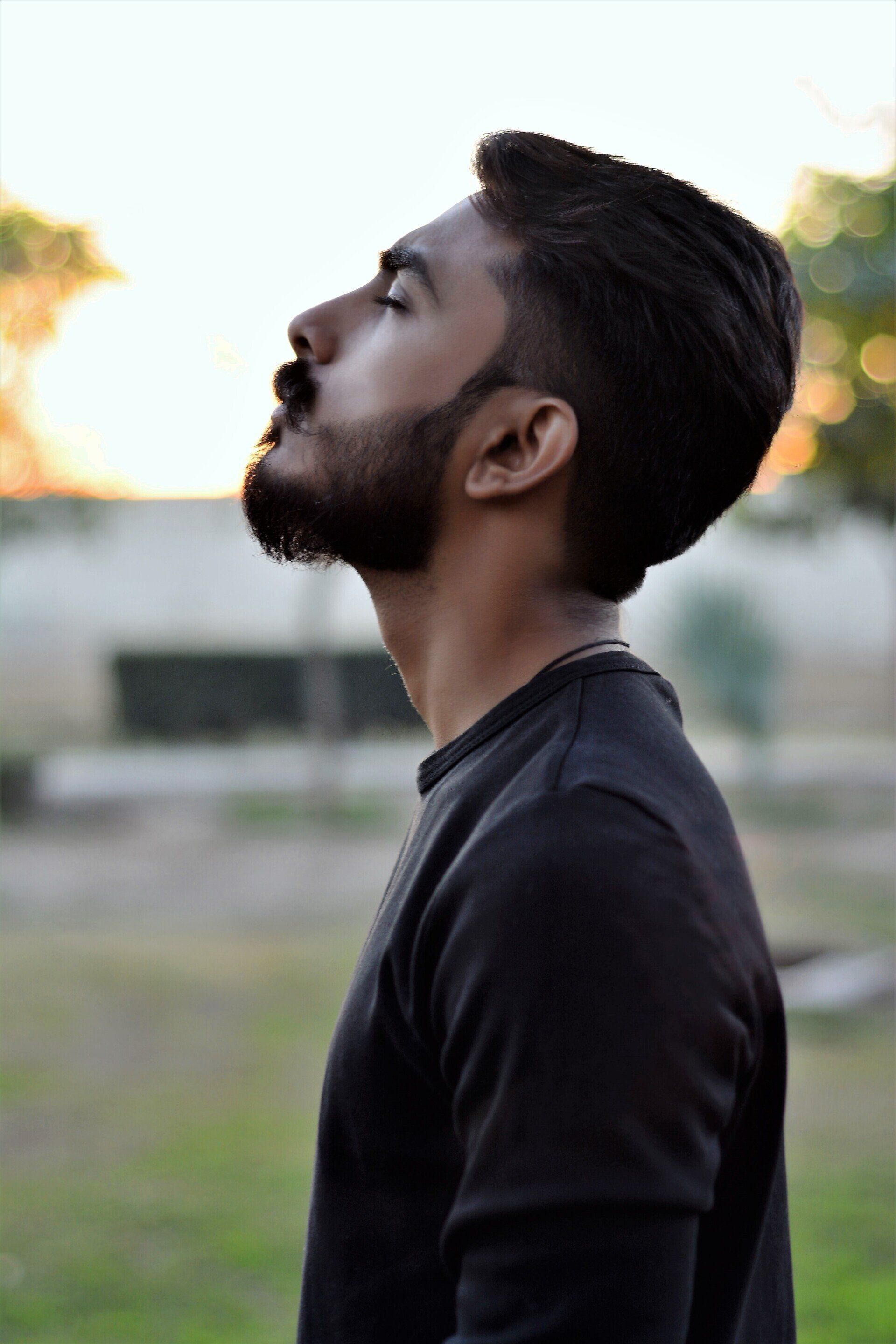 A man with a beard is looking up with his eyes closed.