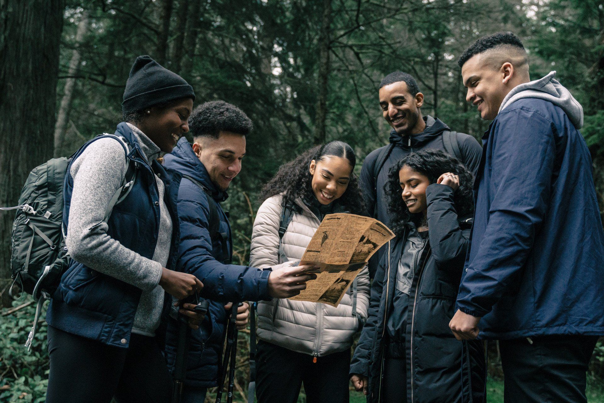 A group of happy hikers looking at a map and standing in the middle of the woods.