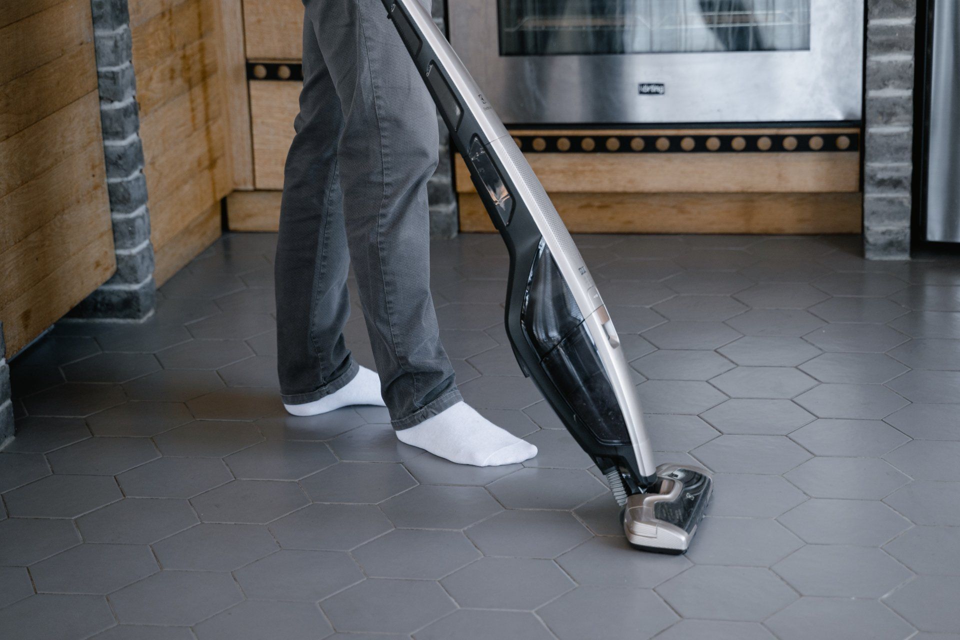 A person is using a vacuum cleaner to clean the floor in a kitchen.