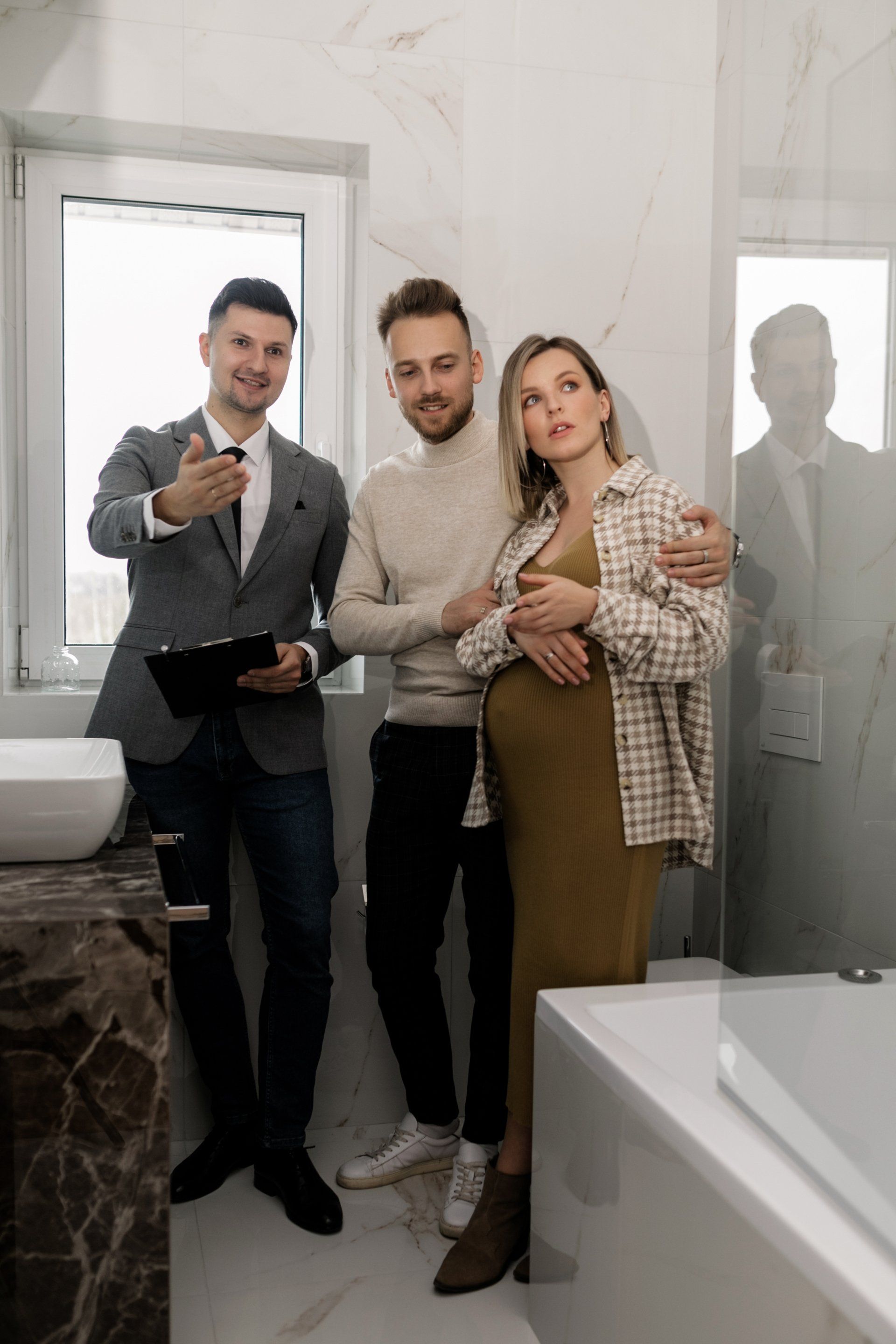 A pregnant woman is standing next to two men in a bathroom.