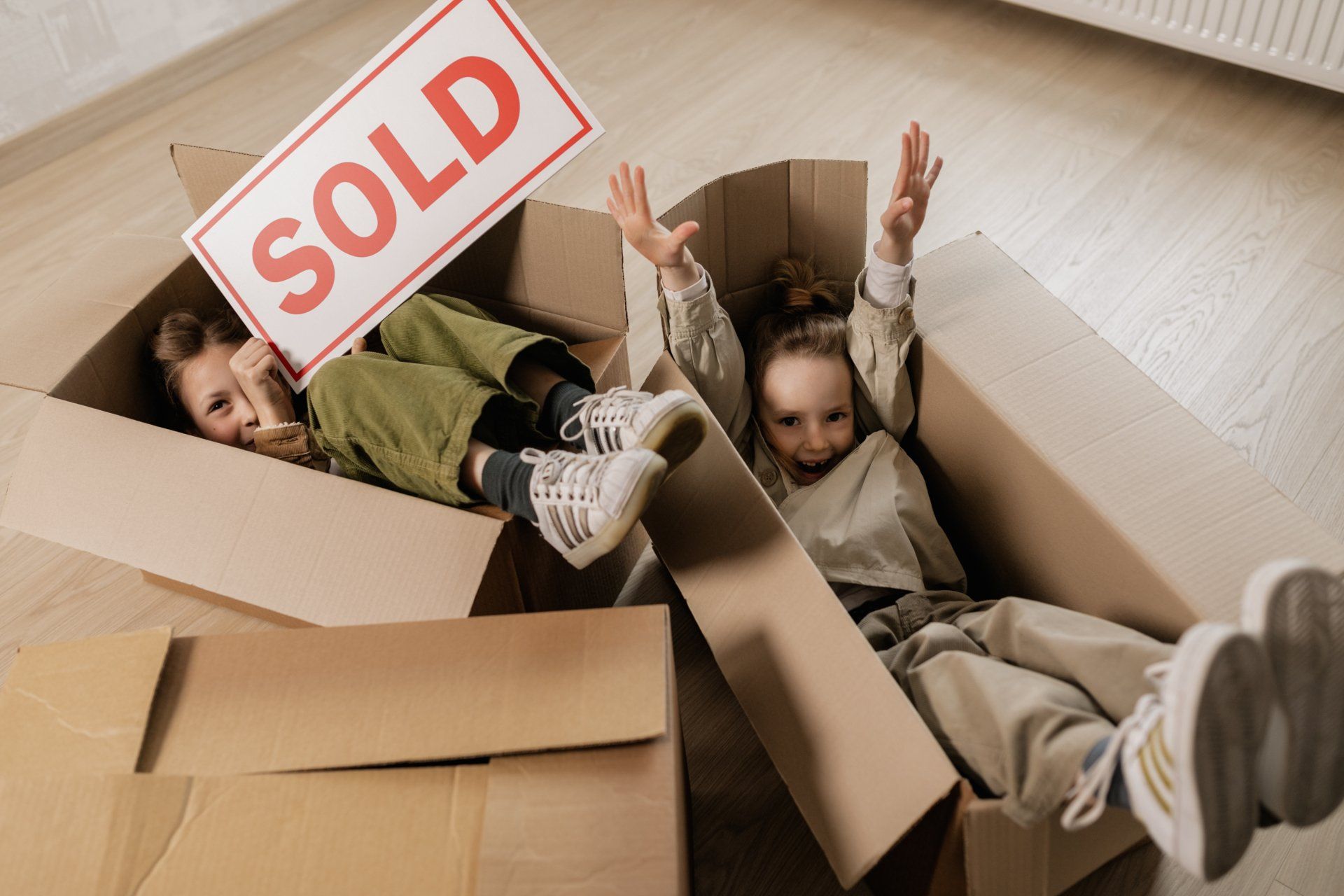 two children are sitting in a cardboard box holding a sold sign .