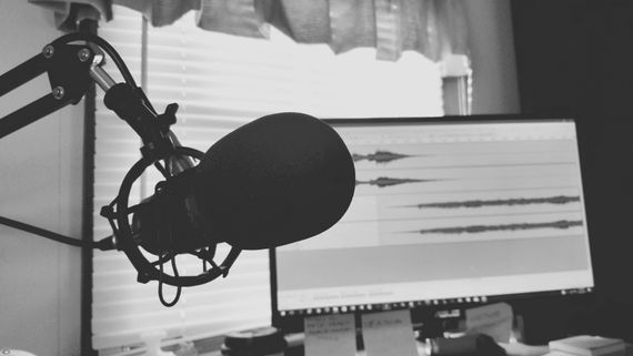 black and white image of a podcast microphone in front of a sound editing monitor.