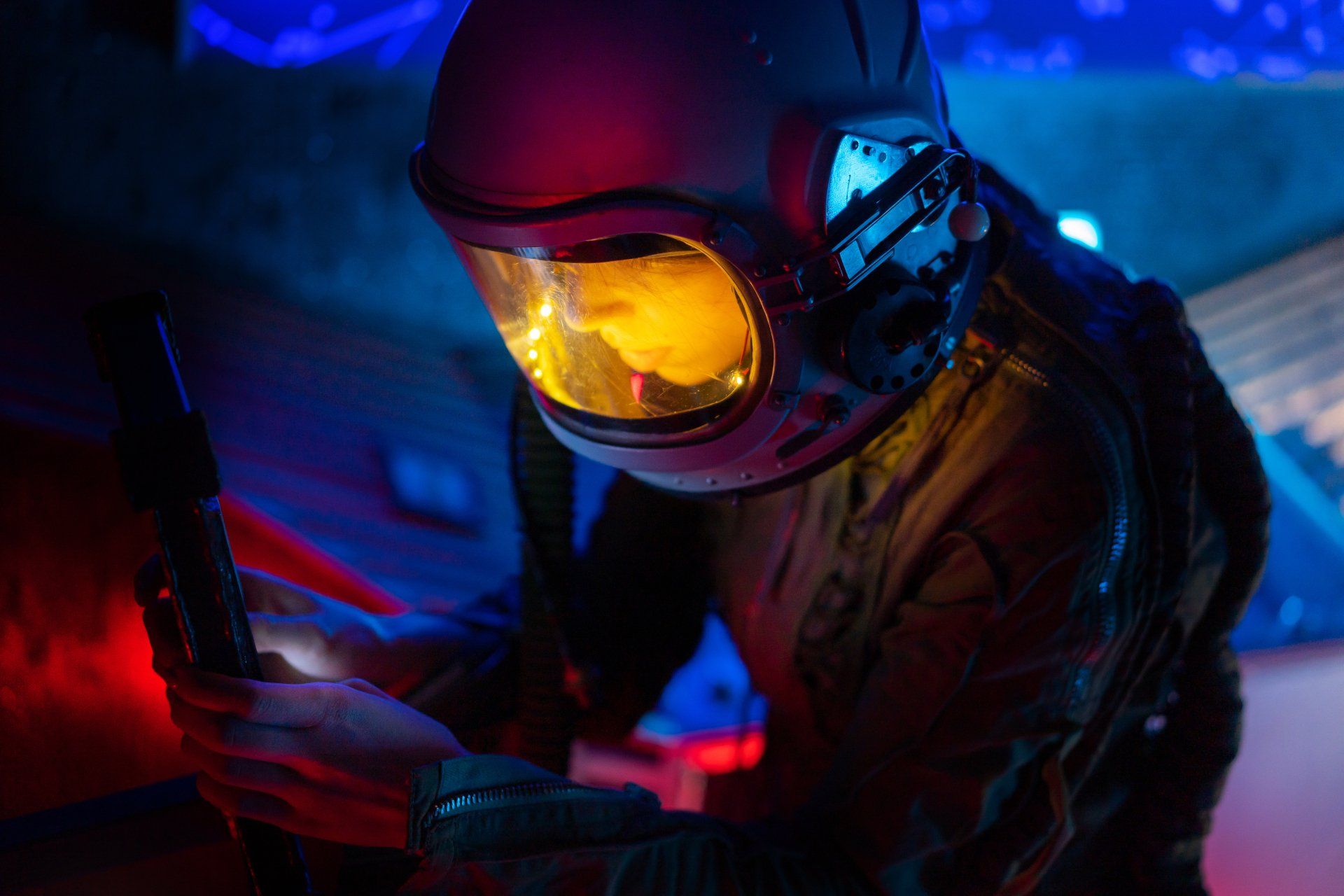 Astronaut in helmet, illuminated by red and blue light, holding a control, inside a spacecraft.