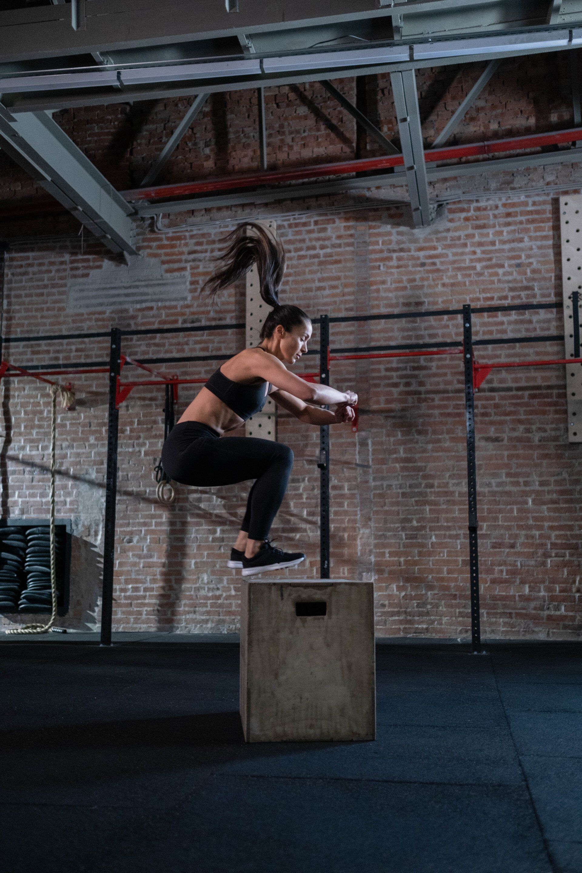 a woman is jumping on a box in a gym .