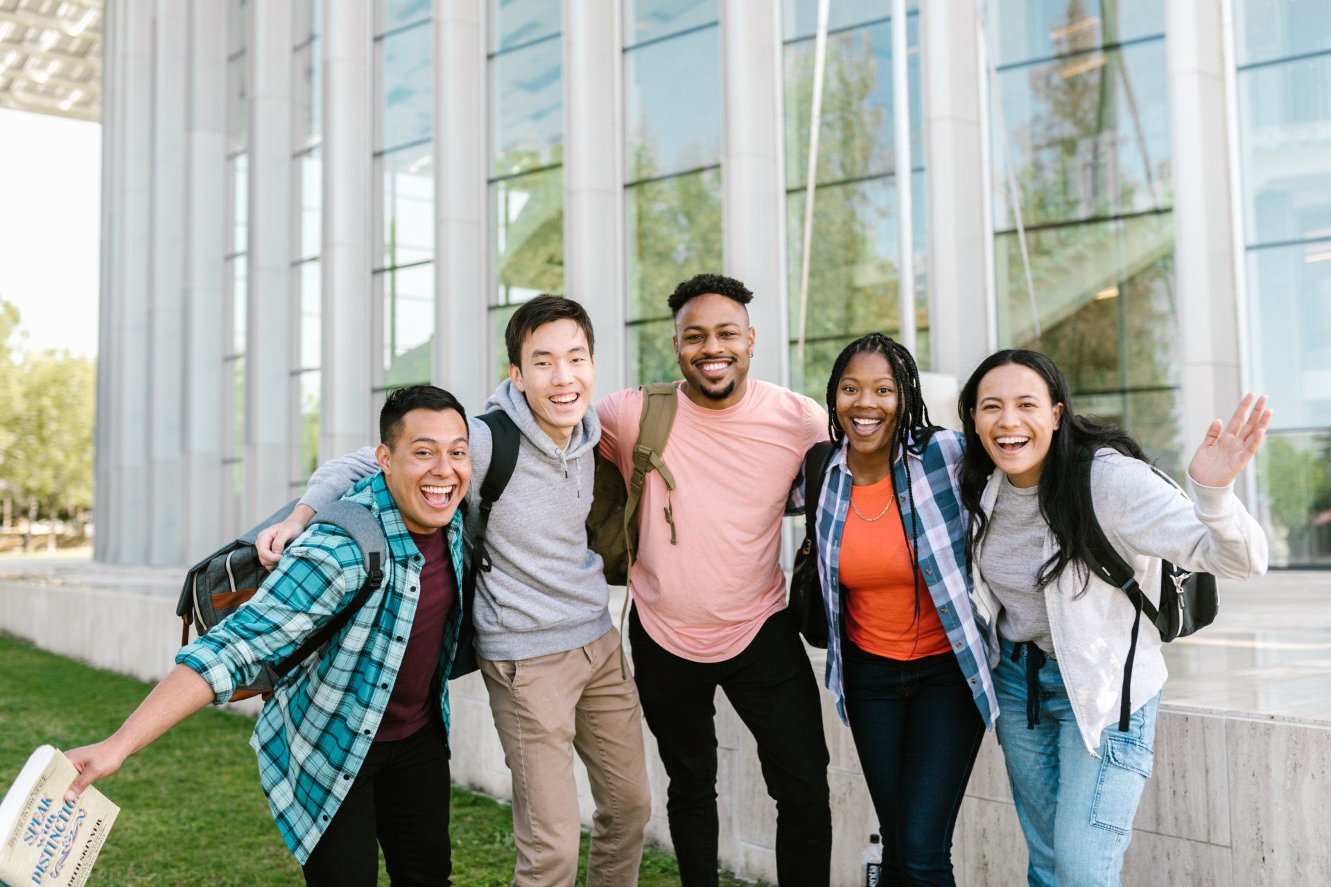 Five diverse students smile and pose in front of a modern building.