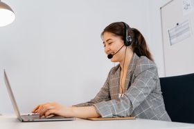 A woman wearing a headset is sitting at a desk using a laptop computer.