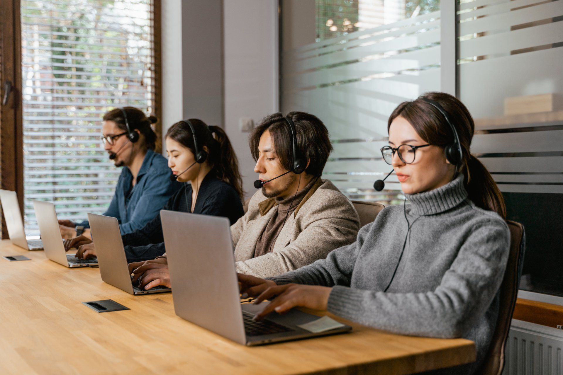 A group of people are sitting at a table with laptops and headsets.