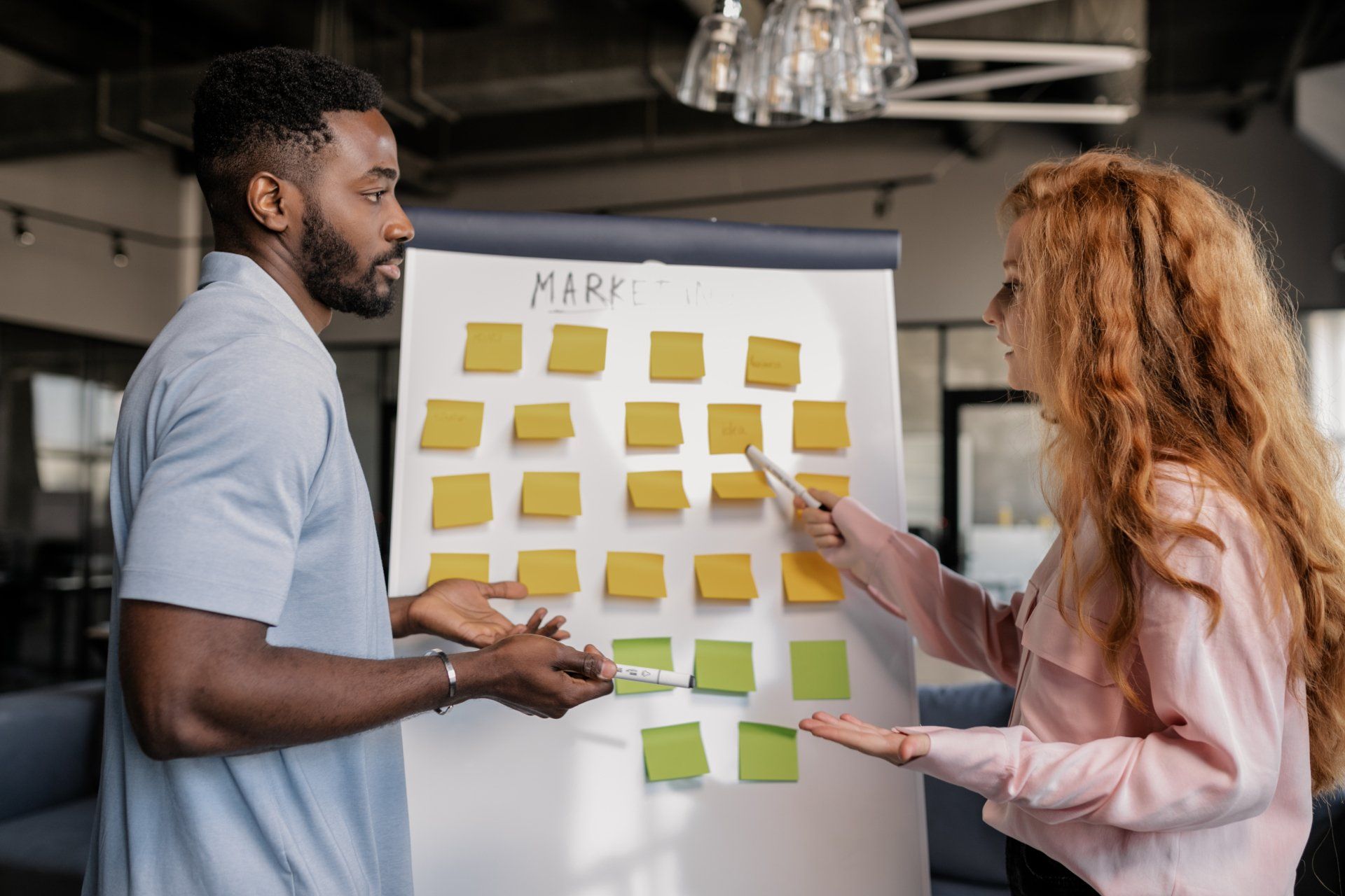 A man and a woman are standing in front of a whiteboard with sticky notes on it.