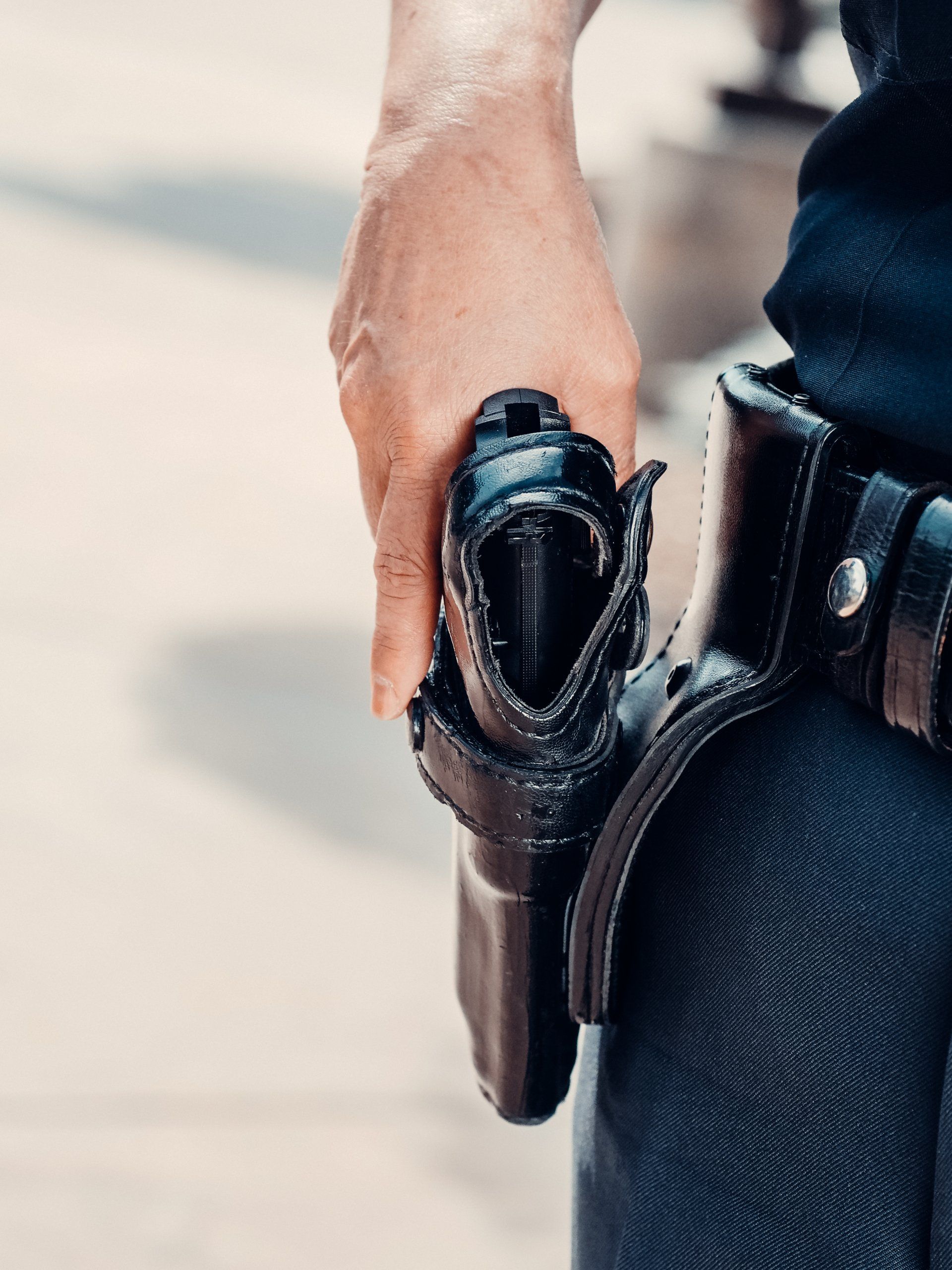 A person's hand gripping a black pistol in a leather holster attached to a belt.