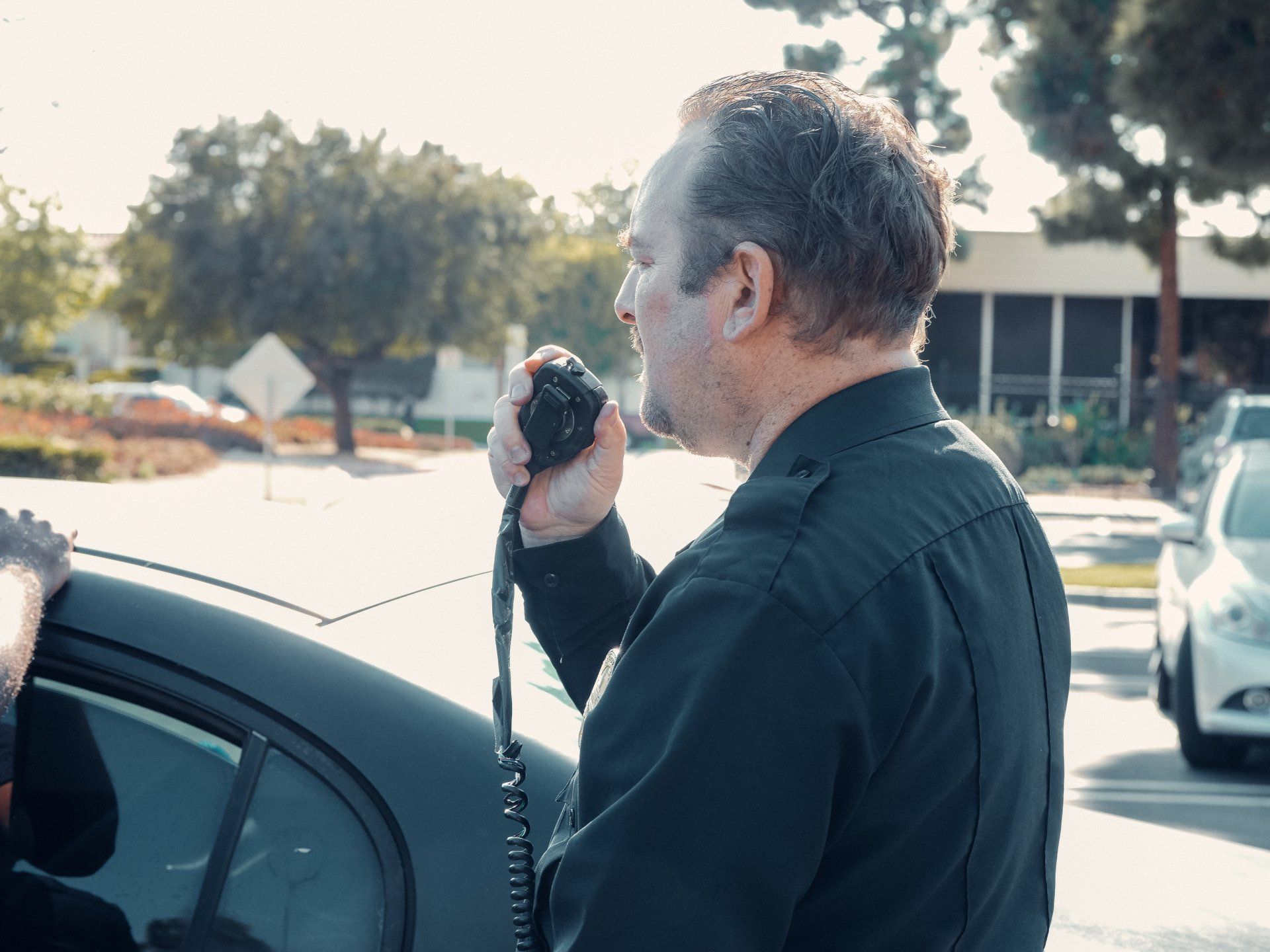 A man is talking on a walkie talkie next to a car.