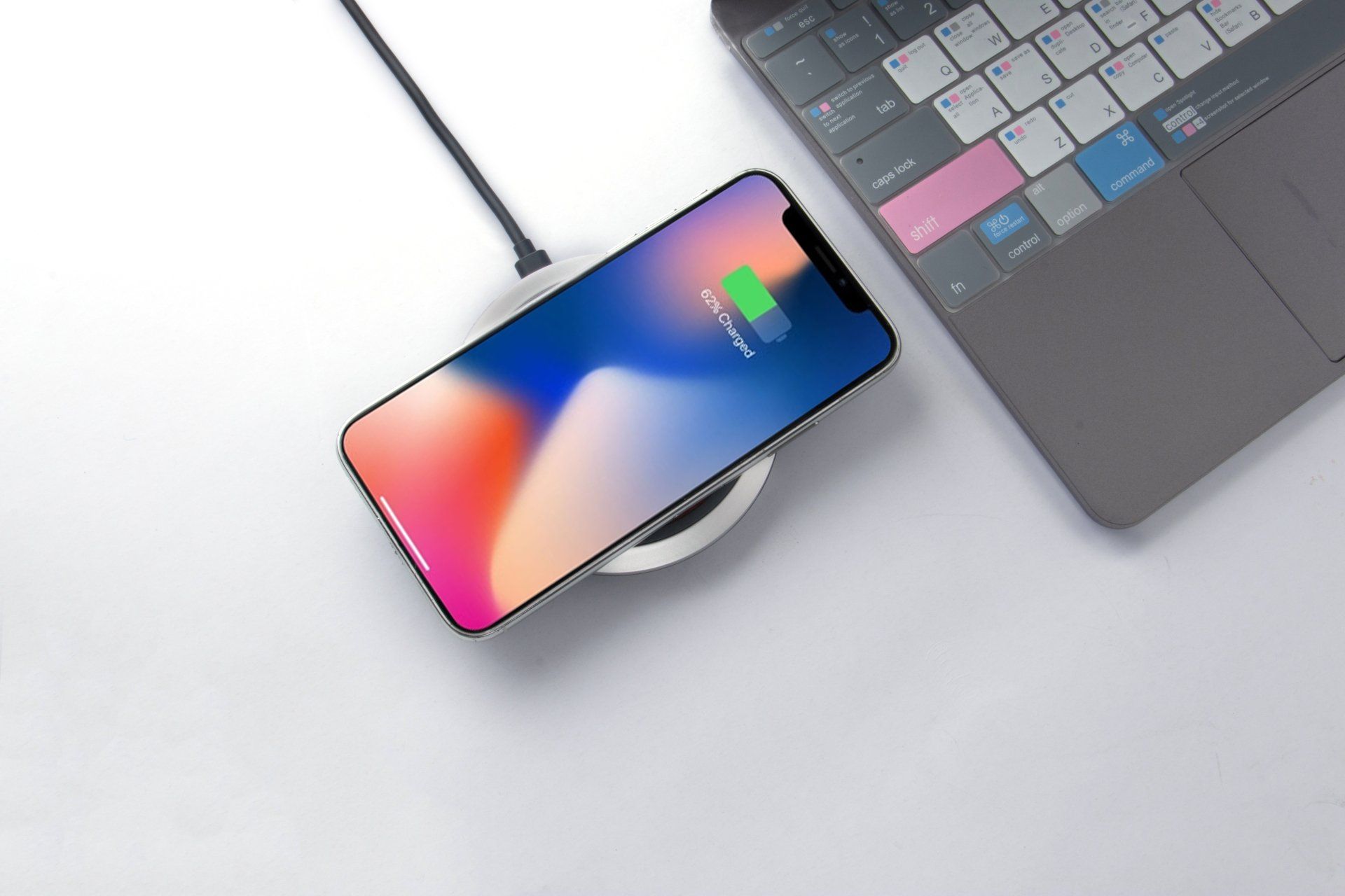 An iphone x is charging on a wireless charger next to a laptop