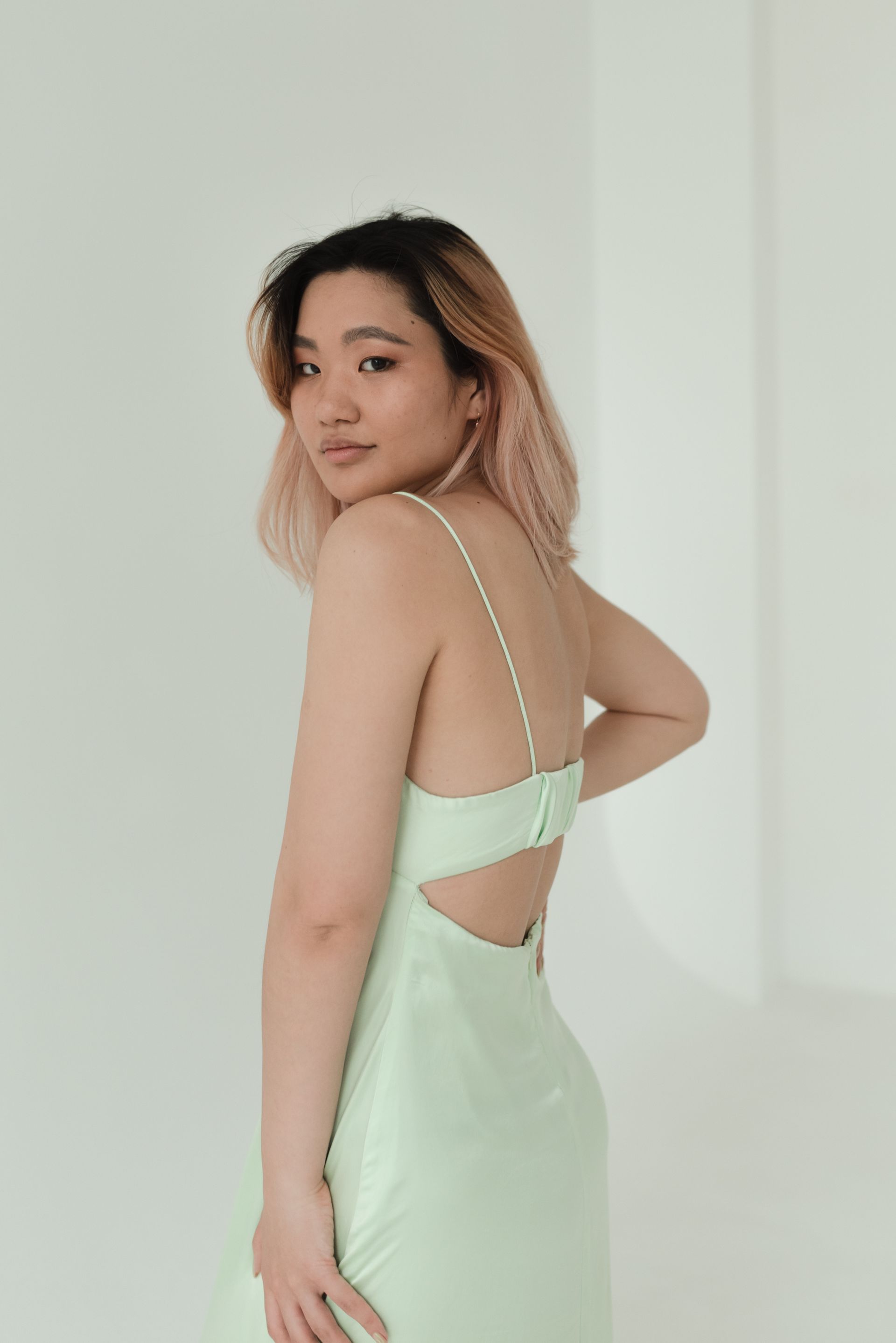 A woman in a green dress is standing in front of a white wall.