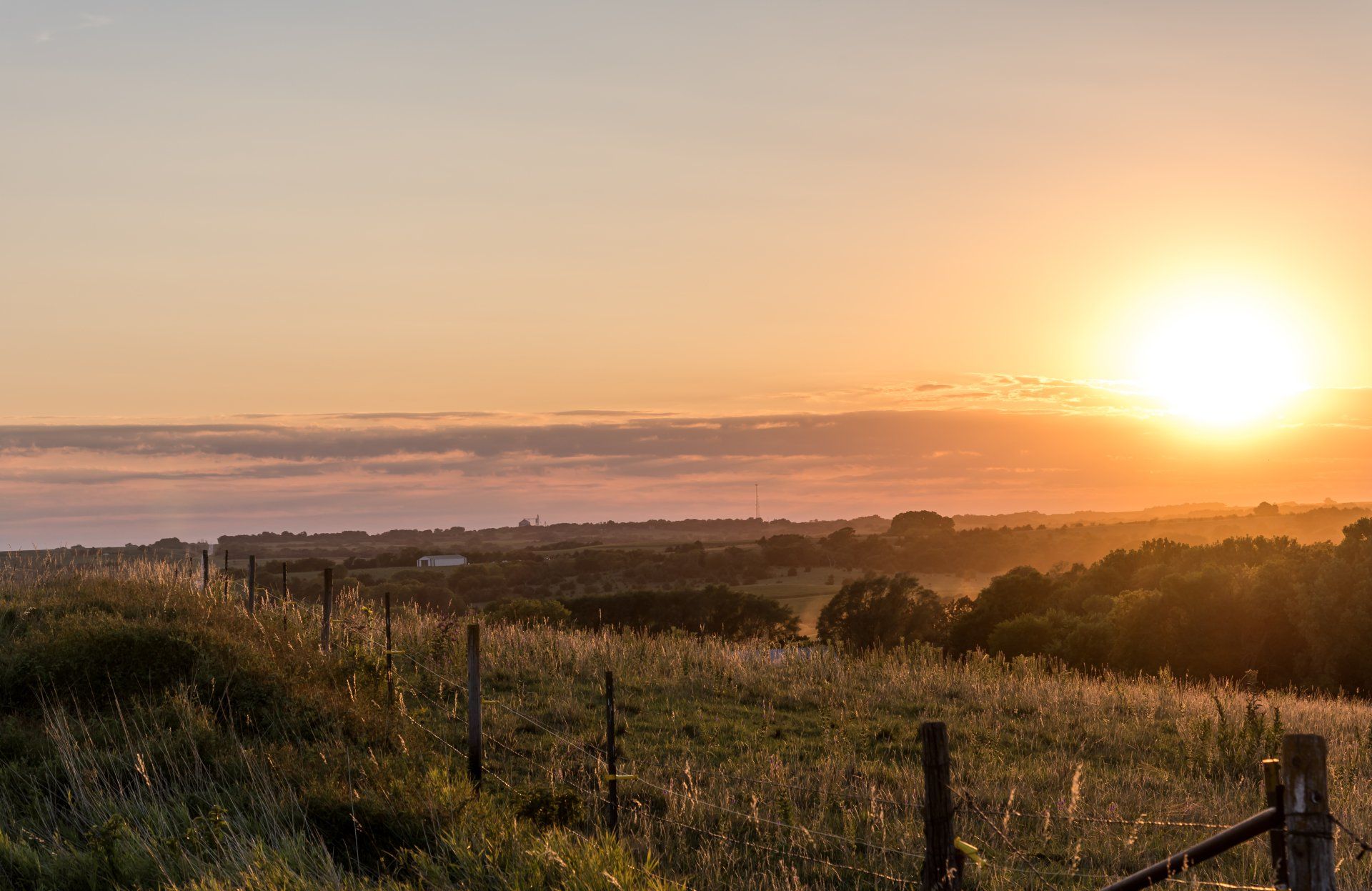 The sun is setting over a field with a fence in the foreground.