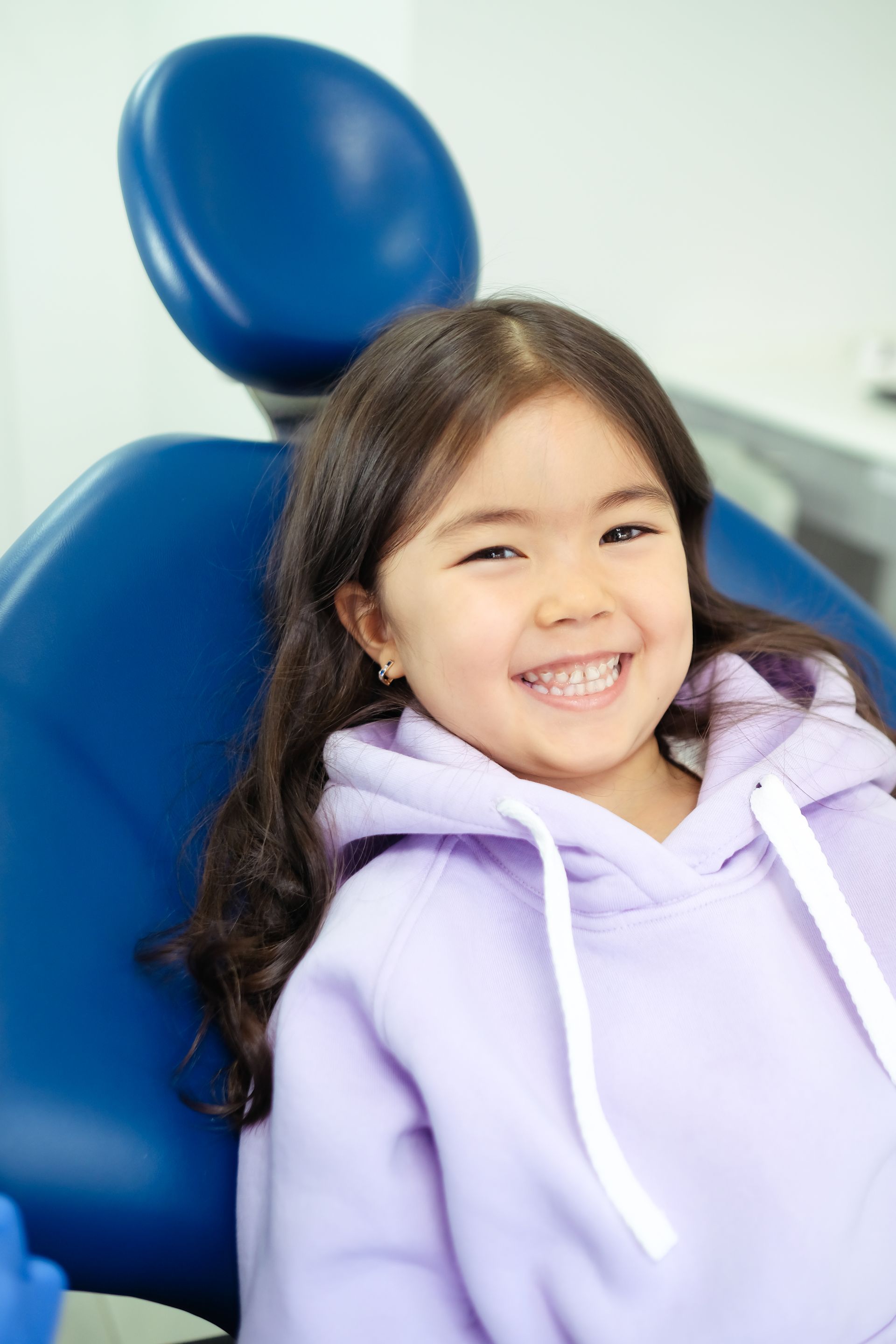 A little girl is sitting in a dental chair and smiling.