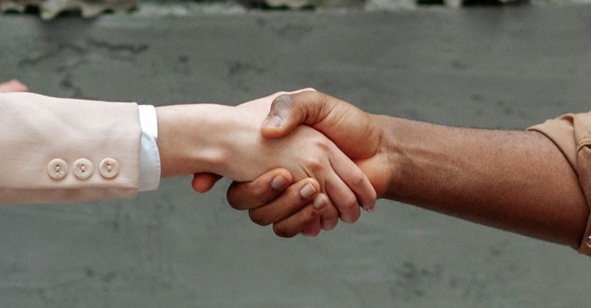 A man and a woman are shaking hands in front of a wall.