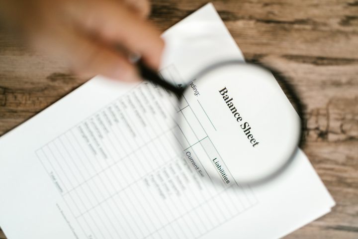 a person is holding a magnifying glass over a balance sheet .