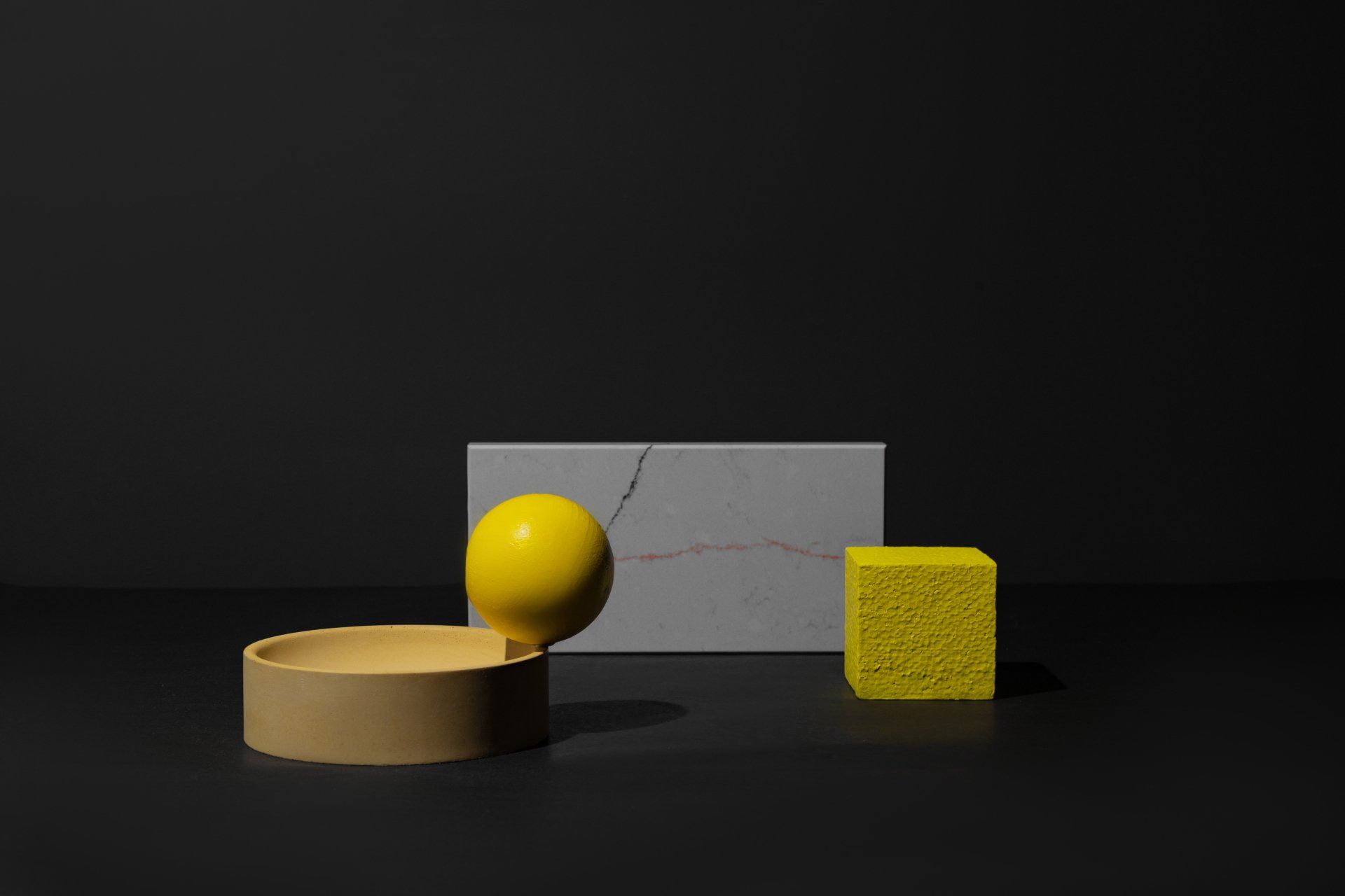 Une balle jaune, un cube jaune et une éponge jaune sont posés sur une surface noire.