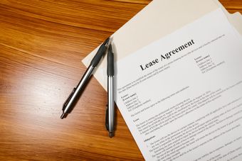 A lease agreement is sitting on a wooden table next to two pens.