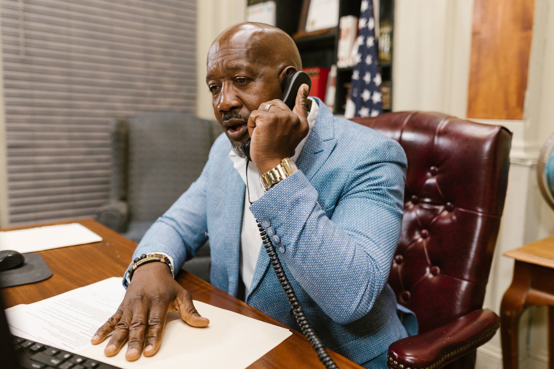 Black man in a suit sitting in a leather chair holding an office phone to his ear