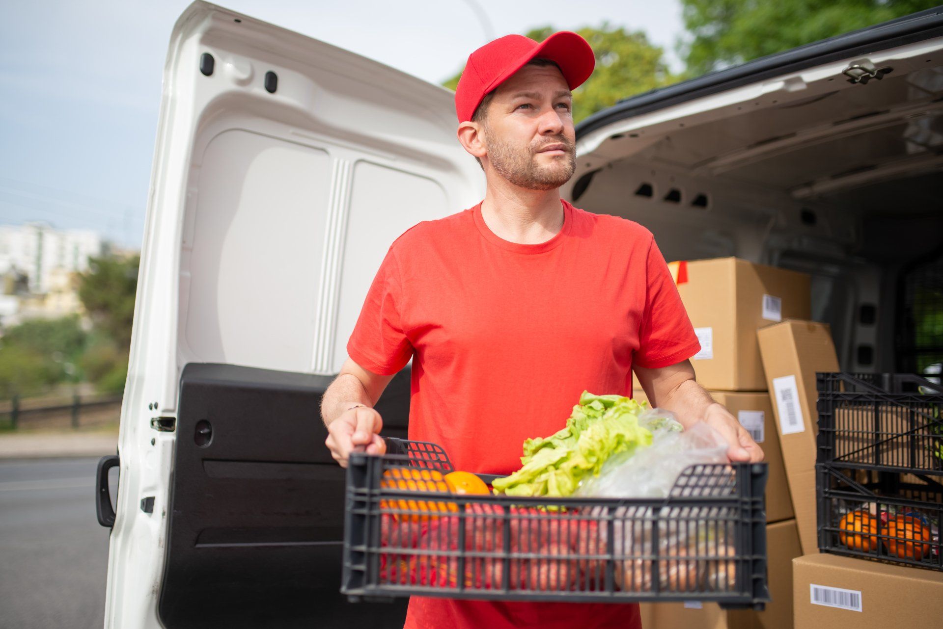 A delivery man is holding a crate of vegetables in front of a van.