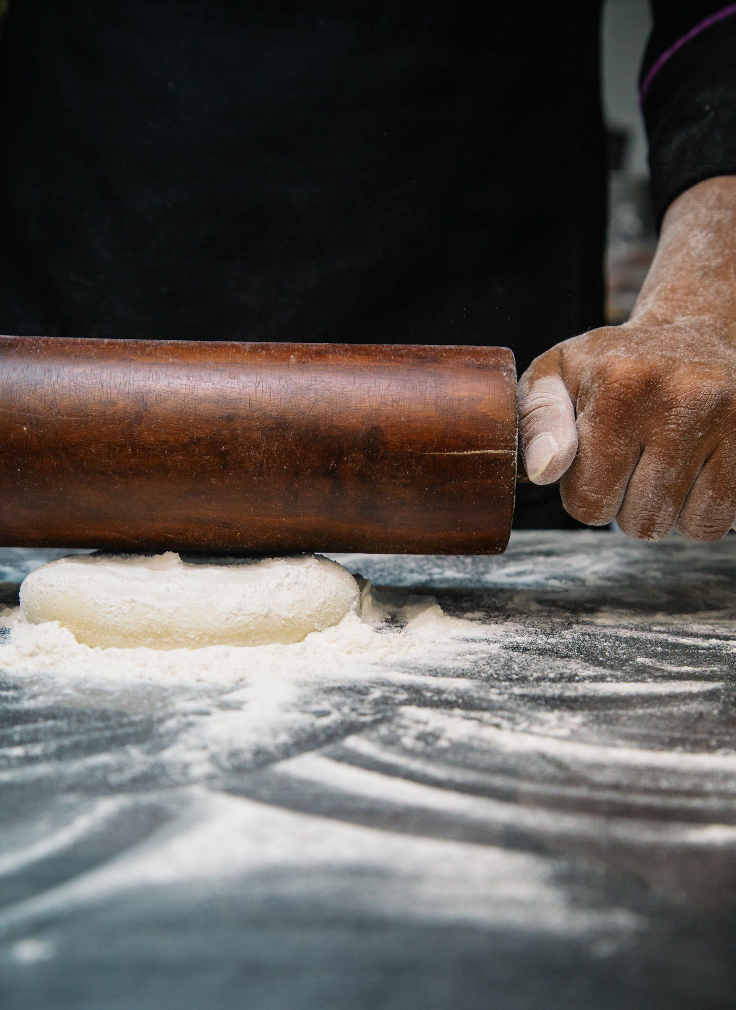 A person is rolling dough with a wooden rolling pin.