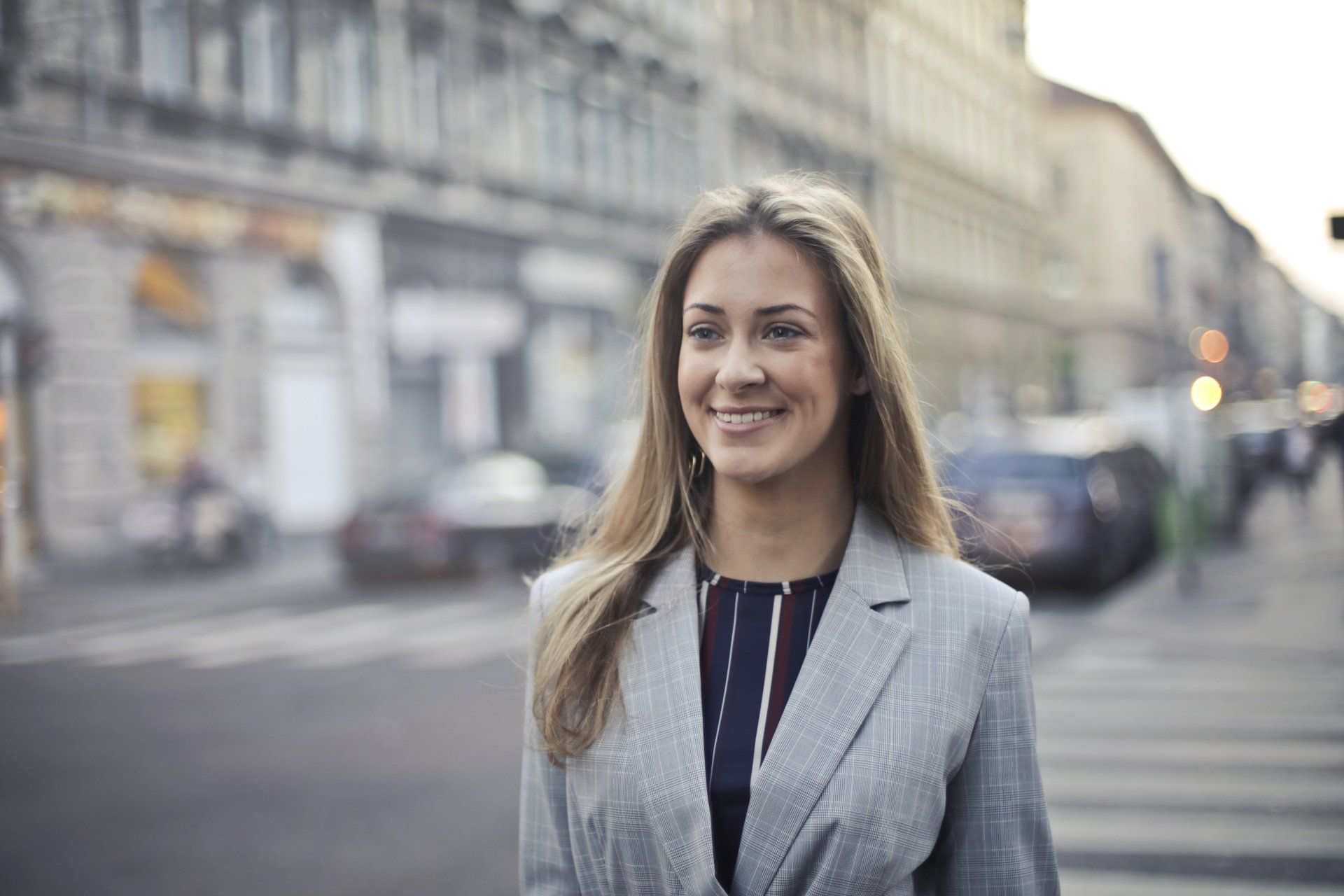 A woman in a suit is walking down the street and smiling.