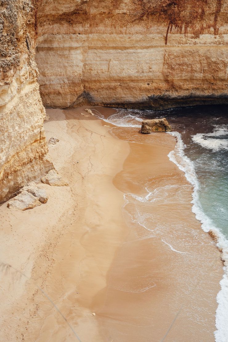 A large secluded beach with tall cliffs surrounding it, and the ocean water lapping at the beach