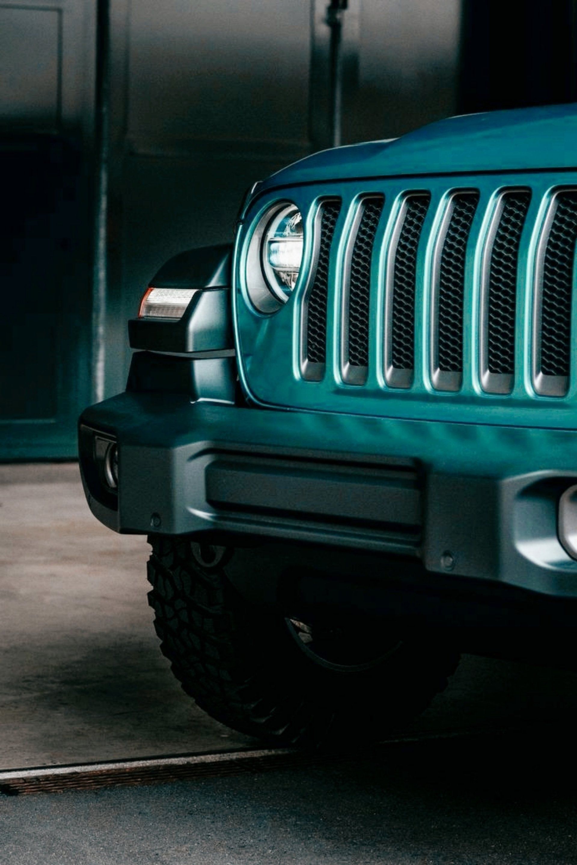 The front of a blue jeep is parked in a garage.