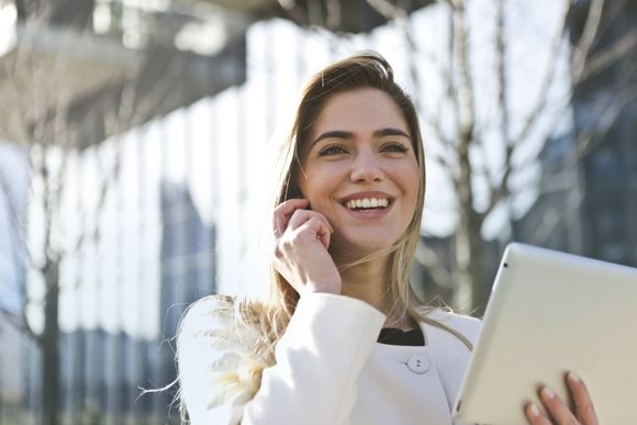 A woman is holding a tablet and talking on a cell phone.