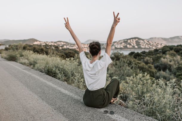 A woman is sitting on the side of a road with her arms in the air.