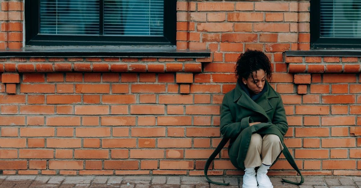 A black woman in Atlanta is sitting on the ground in front of a brick wall
