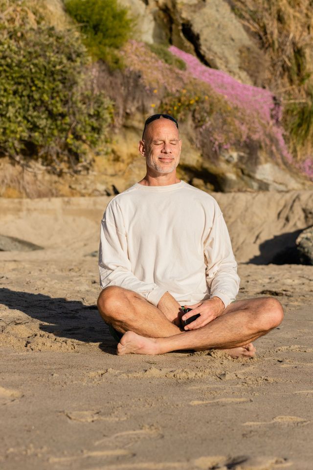 A man is sitting in a lotus position on the beach.