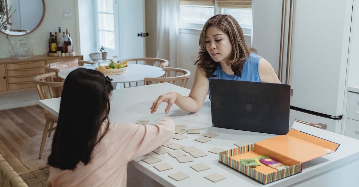 Mom Working on laptop in kitchen and helping daughter with an activity