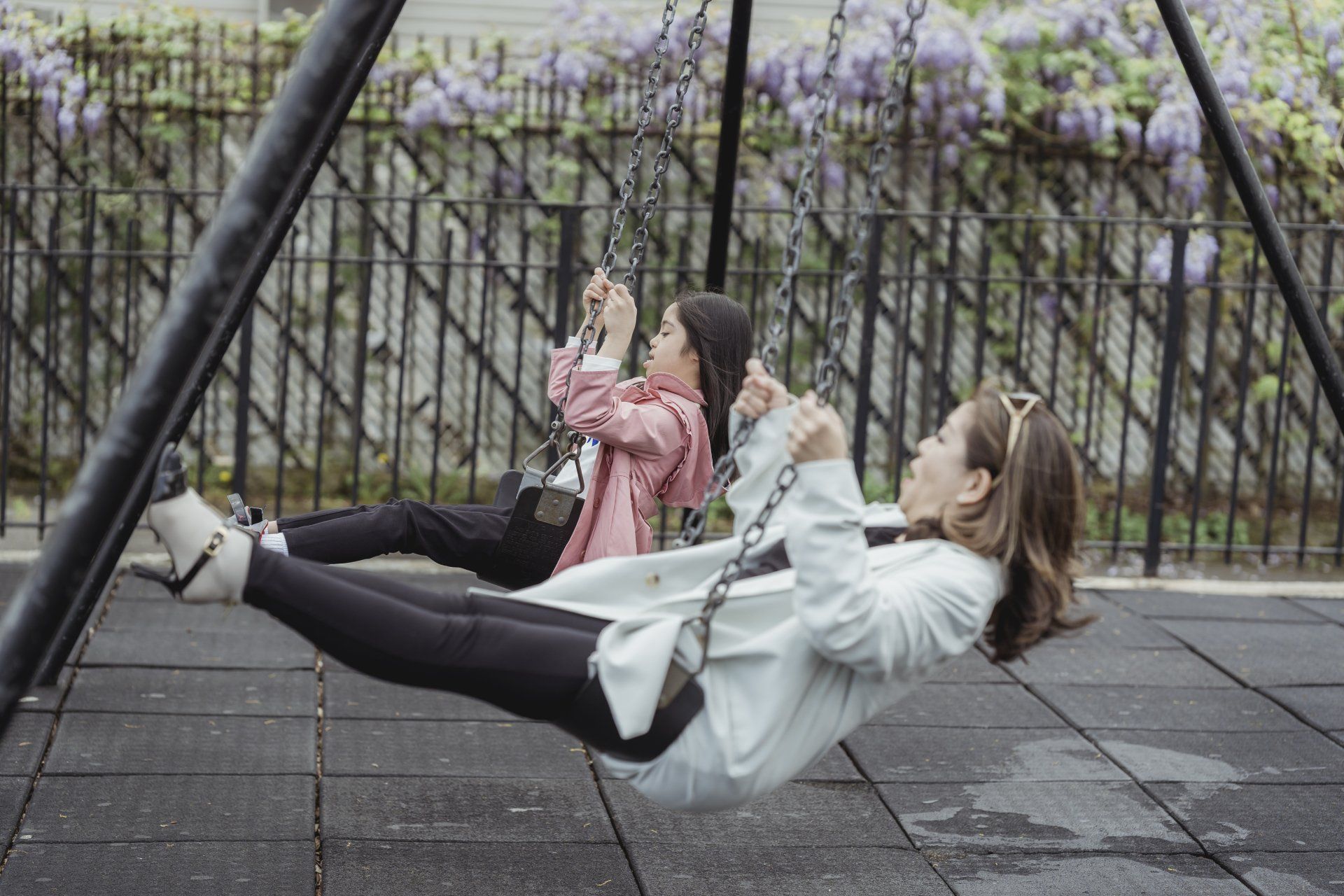 Two girls are swinging on a swing set in a park.